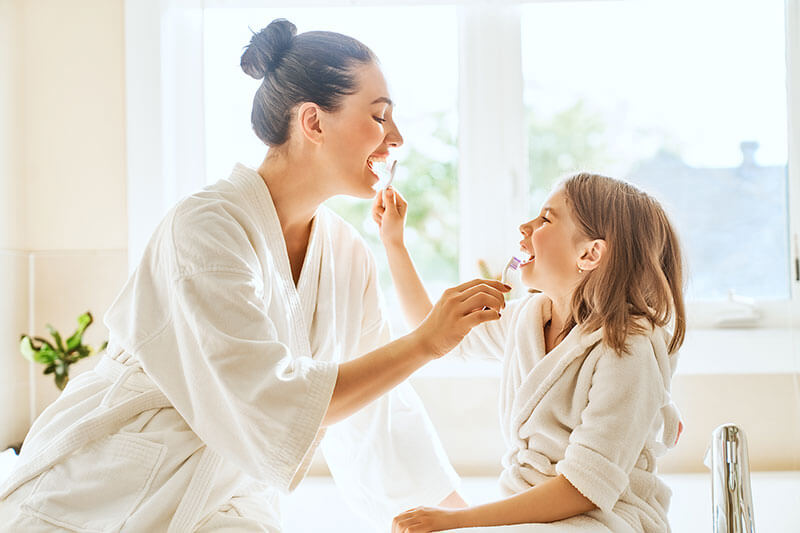 Mother showing her daughter how to brush her teeth