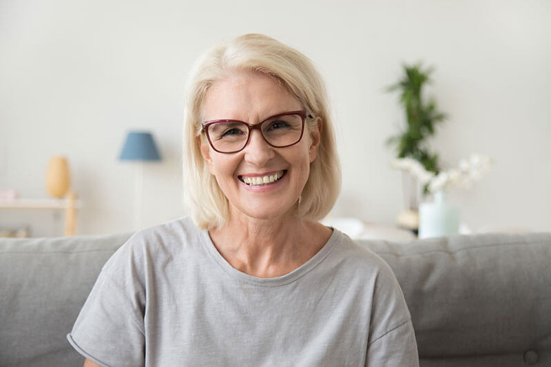 A woman with glasses smiling on her couch